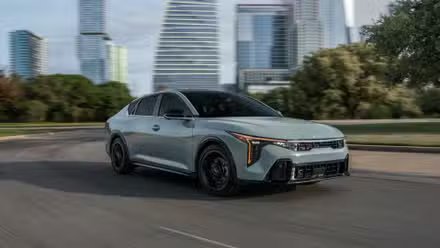 Vue 3/4 avant d'une Kia K4 2025 grise traversant une ville.