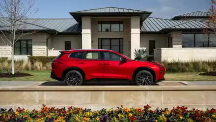 Photo de profil latérale statique d'une Toyota Crown Signia Limited 2025 rouge garée à l'extérieur d'une maison.