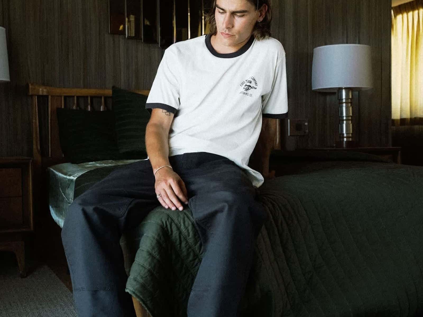 Mannequin assis sur un lit de motel portant le t-shirt Ford Mustang Ringer en blanc Wimbledone