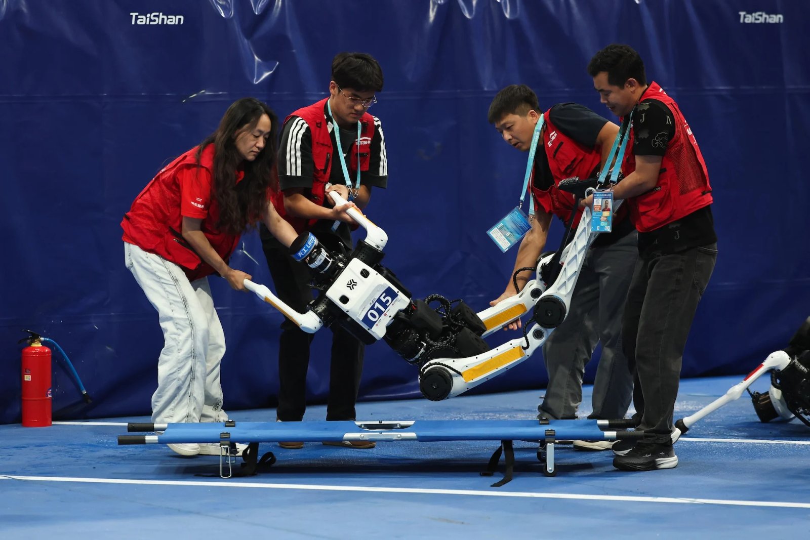 Les membres de l'équipe de maintenance utilisent une civière pour déplacer un robot humanoïde après sa chute dans une course de 100 mètres lors des 2e Jeux mondiaux du robot humanoïde à l'Anneau national de patinage de vitesse le 25 août 2026 à Pékin, en Chine. 