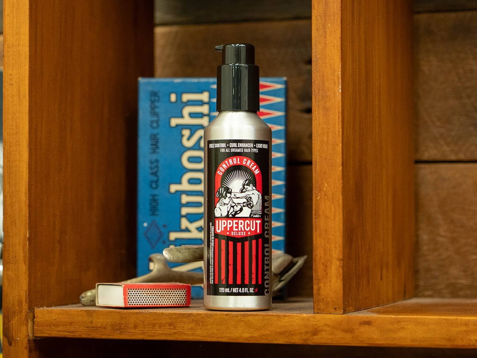 La bouteille de Control Cream sur une étagère en bois à côté d'une boîte de tondeuse à cheveux Kikuboshi vintage et d'une boîte d'allumettes.