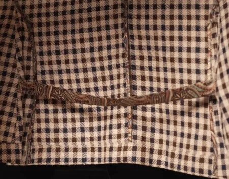 Vidéo Highlight 3 Veste à carreaux avec sangles d'aération Gros plan sur la fente arrière d'un manteau de sport à carreaux, avec une sangle en tissu à motifs reliant les deux bords de la fente