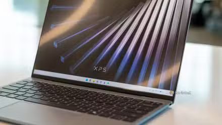 Gros plan sur l'écran incliné du Dell XPS 13 avec fond d'écran XPS et barre des tâches Windows.