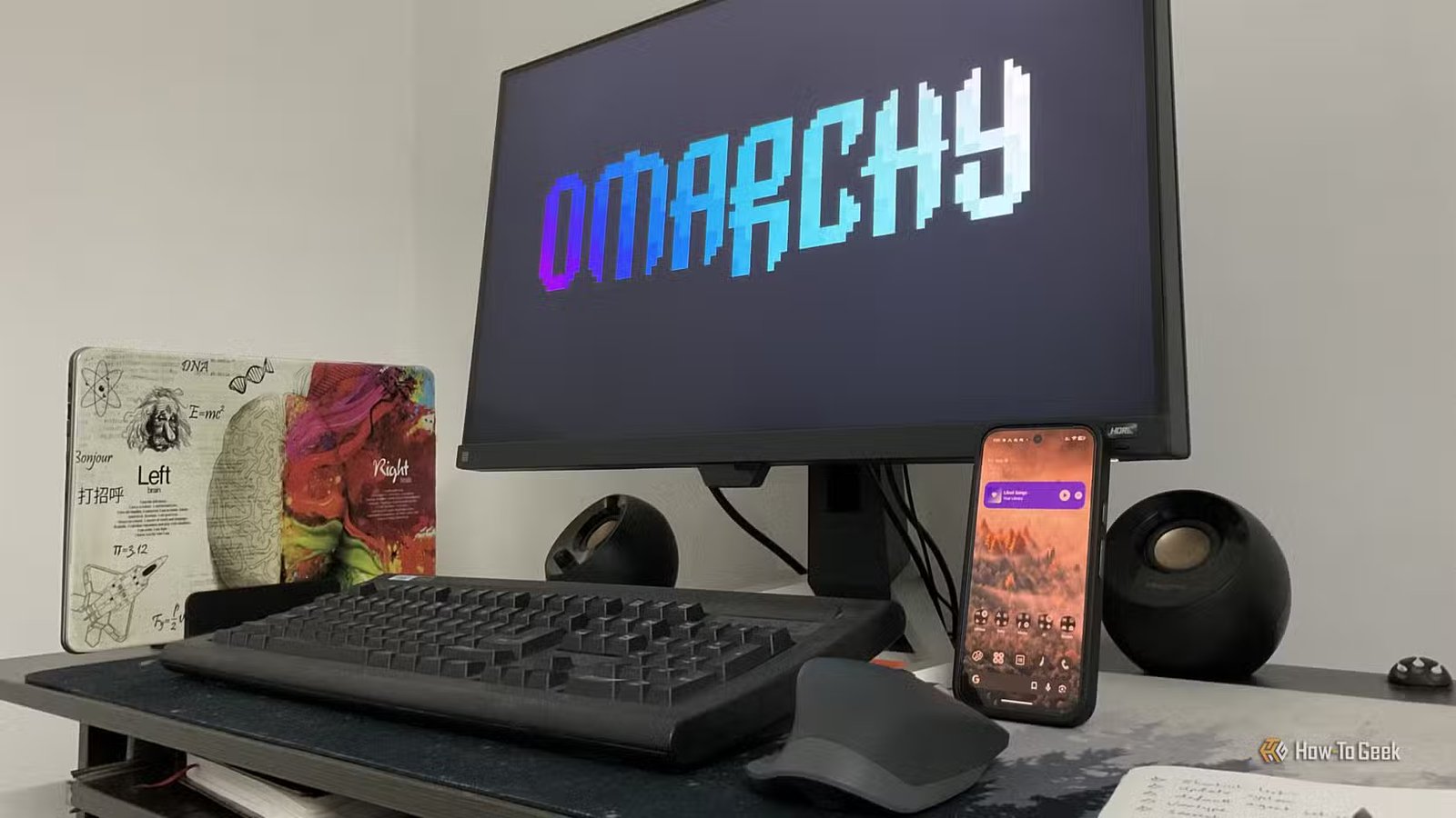 Logo de démarrage Omarchy sur un écran de bureau avec clavier, souris et téléphone dans le cadre.