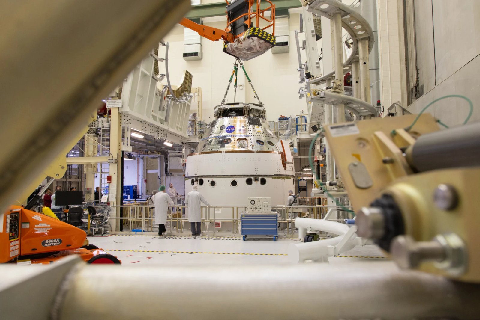 Une grue ramène le vaisseau spatial Artemis II Orion de la NASA à la cellule d'assemblage final et de test du système (FAST) à l'intérieur du bâtiment Neil A. Armstrong des opérations et des caisses du Centre spatial Kennedy de la NASA en Floride, le vendredi 21 mars 2025, après l'installation de quatre vents de panneaux solaires et de carénages de largage d'adaptateur.