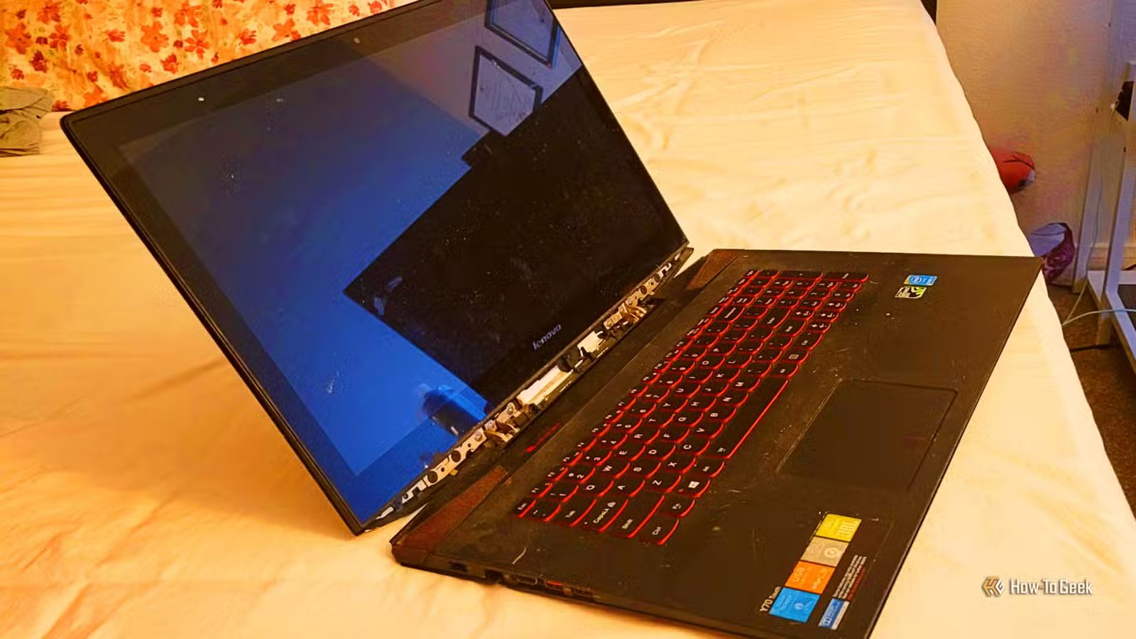 Un ordinateur portable Lenovo posé sur un lit, allumé avec un écran noir.