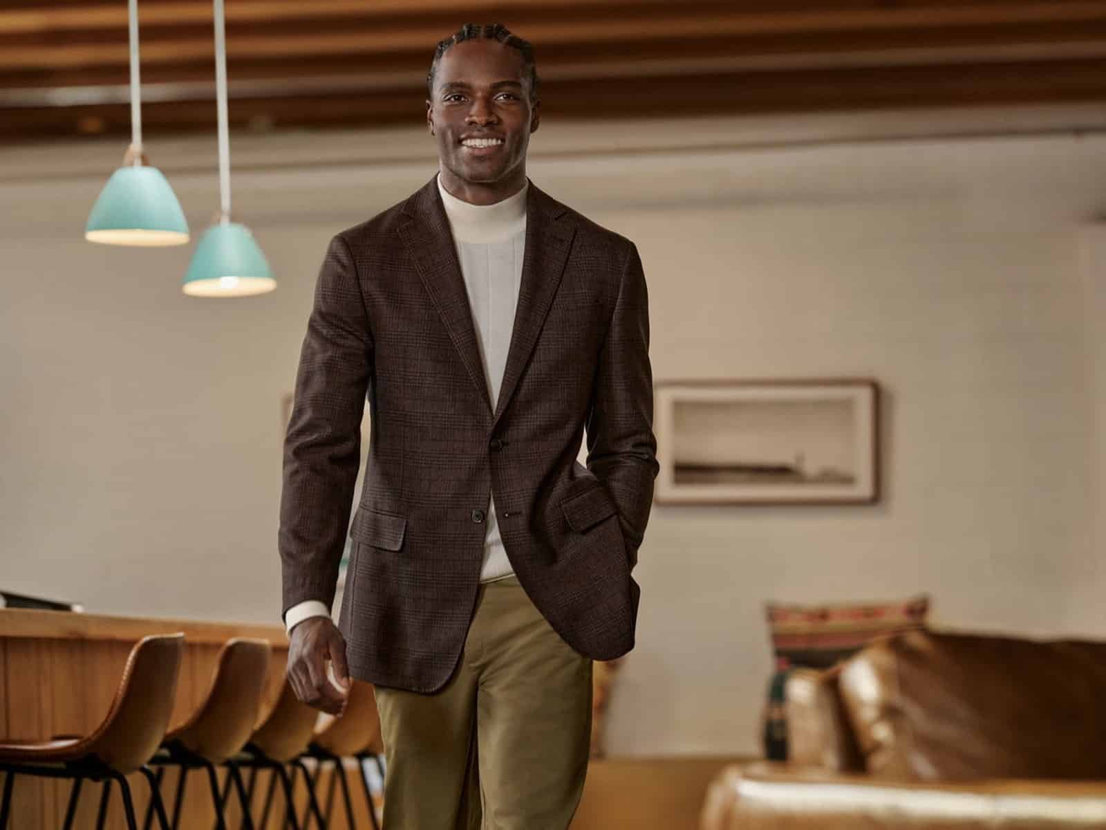 Un homme vêtu d'un manteau de sport à carreaux marron, d'un col roulé blanc et d'un pantalon chino dans un bureau moderne