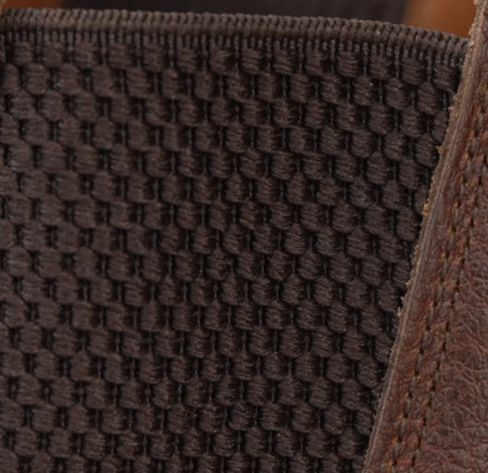 Vidéo d'examen des bottines Chelsea, point culminant 4 Gros plan extrême du panneau latéral élastique texturé en nid d'abeille d'une botte Chelsea marron foncé à côté de la tige en cuir grainé