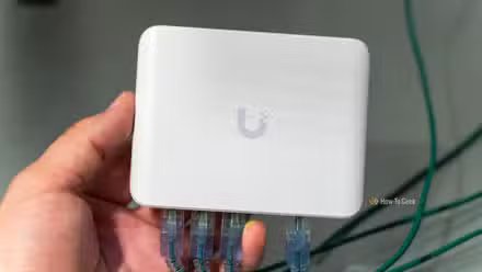 Le commutateur Ethernet Unifi Flex Mini 2,5G avec câbles Ethernet branchés est tenu dans une main.
