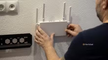 Un homme installant un routeur Wi-Fi blanc sur un mur blanc à côté d'un support TV.