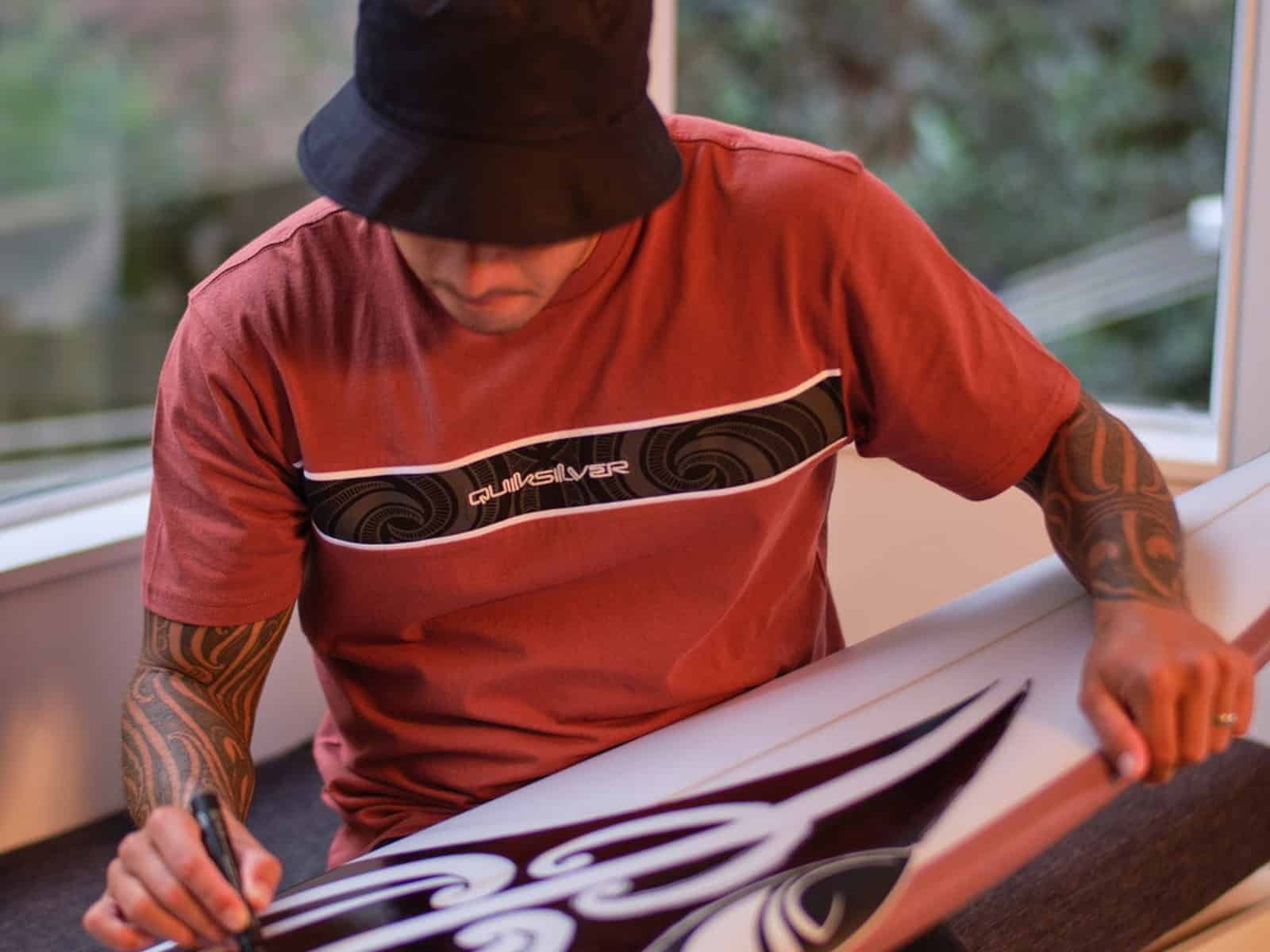 Kehu Butler dessine une œuvre d'art de Tai Kehu sur une planche de surf vierge