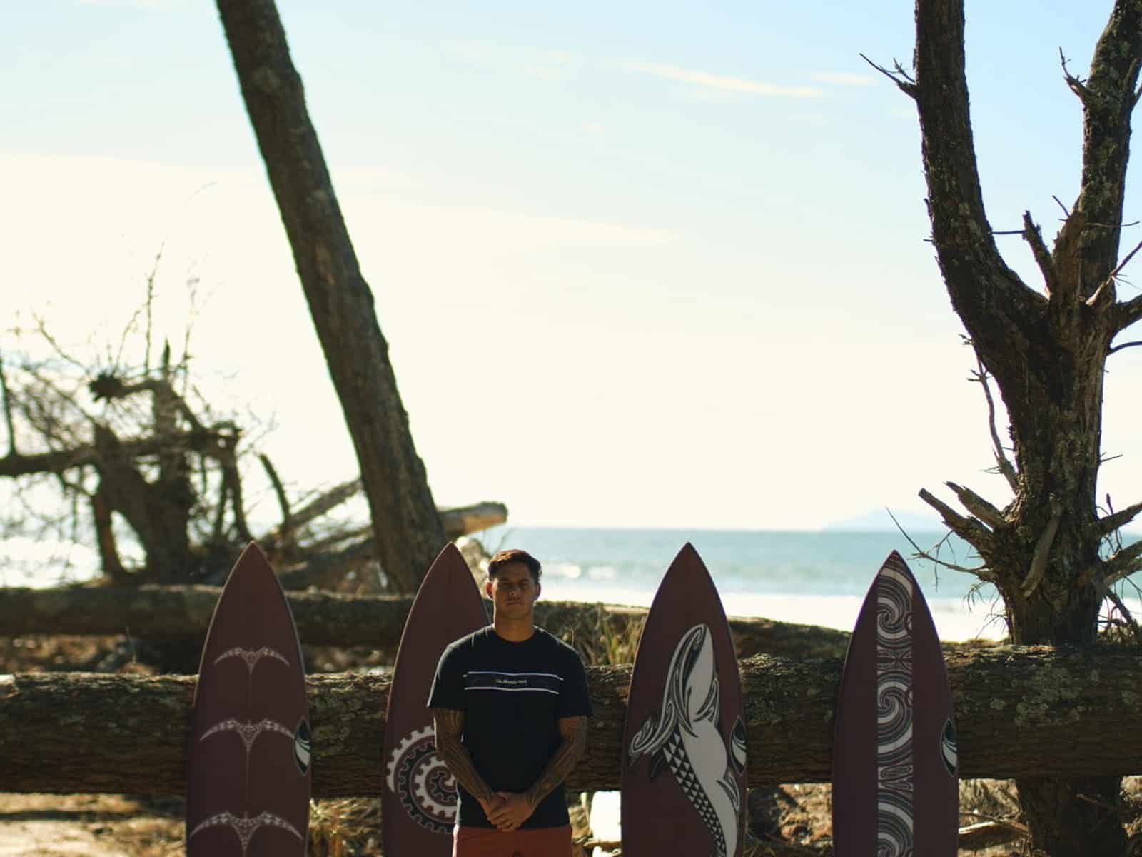 Kehu Butler debout parmi les planches de surf SharpEye Tai Kehu personnalisées sur une plage