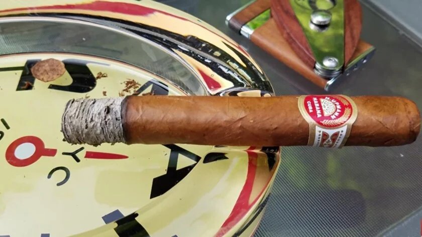 Cendrier à cigares H Upmann cigare H. Upmann allumé avec son bandeau rouge et or « Habana Cuba » repose sur un cendrier à cigares