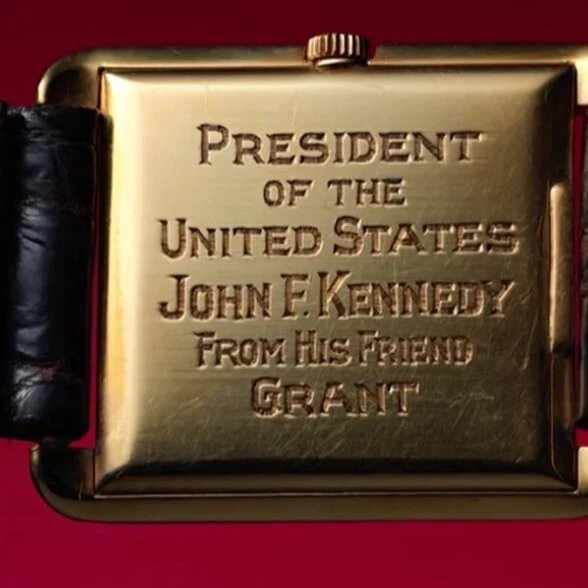 Gravure du fond du boîtier Jfk Omega en vedette Le fond du boîtier en or de la montre Omega de JFK est gravé « Le président des États-Unis John F. Kennedy de la part de son ami Grant », sur un bracelet en crocodile marron sur fond rouge et vert.