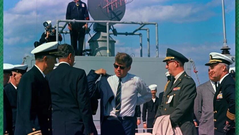 Pince à Cravate Jfk Navire Marine Le président Kennedy en cravate rayée et lunettes de soleil à bord d'un navire de la Marine, discutant avec des officiers en uniforme.