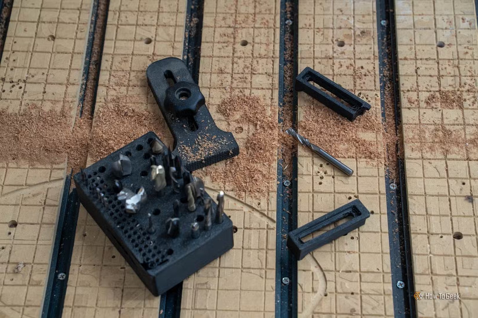 Un porte-embout noir rempli d'embouts de toupie à côté d'une pince de maintien de bouton et de deux pinces CNC imprimées.