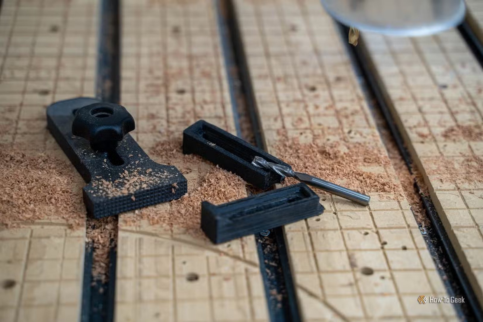 Deux pinces CNC imprimées en 3D, une pince de maintien de bouton et une fraise en bout sur une planche recouverte de sciure de bois.
